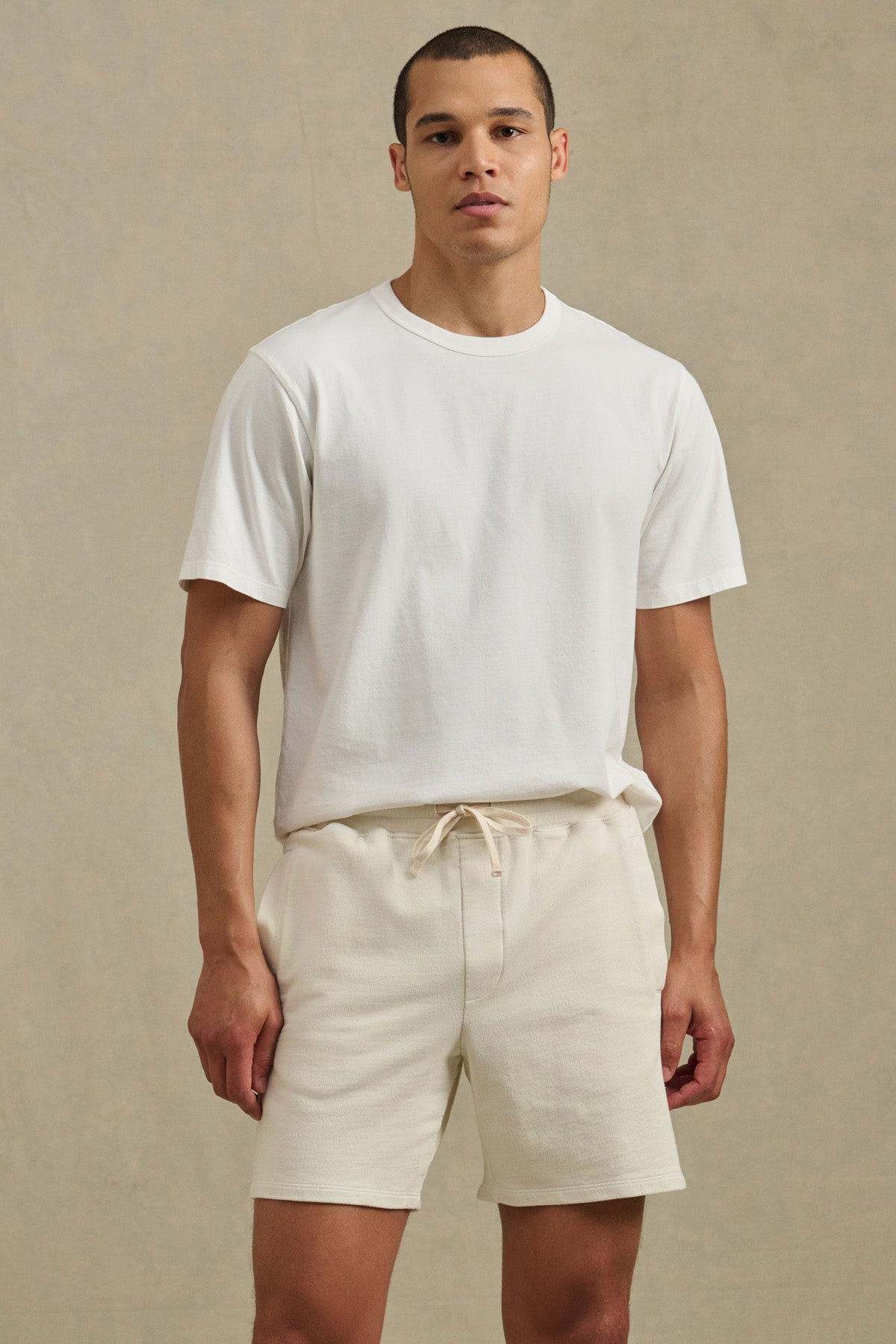 A person stands against a plain background, wearing a white short-sleeve t-shirt and the BOSLOW SHORT by Velvet by Graham & Spencer—relaxed fit shorts with a drawstring waist.-41374357061825