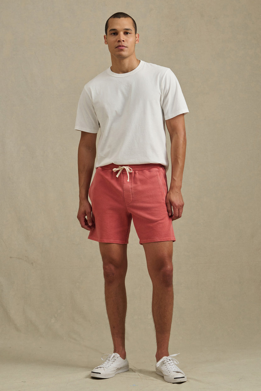 A man stands against a plain background wearing the BOSLOW SHORT in pink by Velvet by Graham & Spencer, styled with a white t-shirt and white sneakers.