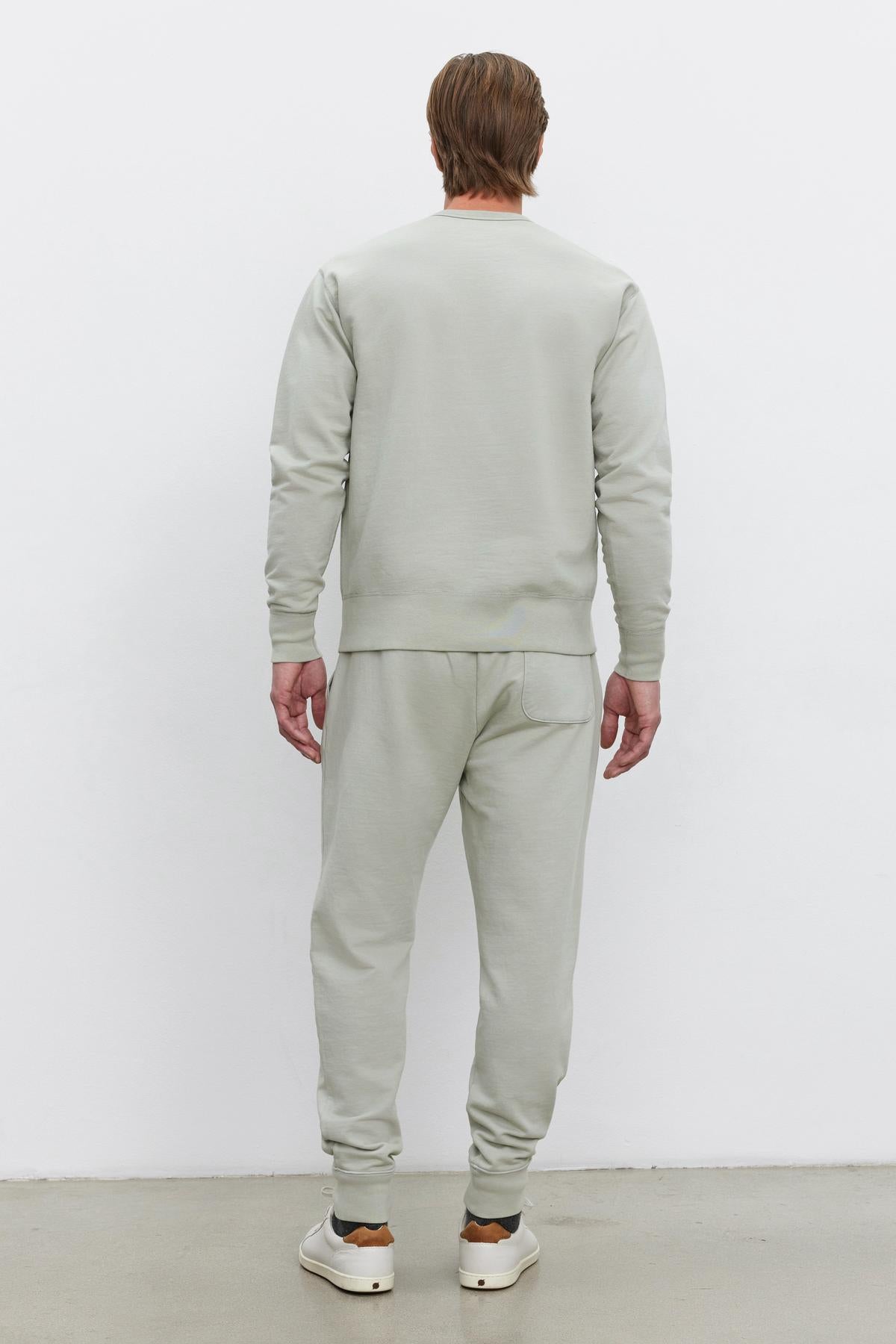   Rear view of a person in a Velvet by Graham & Spencer DUSTY SWEATPANT with an elastic drawstring waist and ribbed cuffs, paired with white sneakers, standing against a white background. 