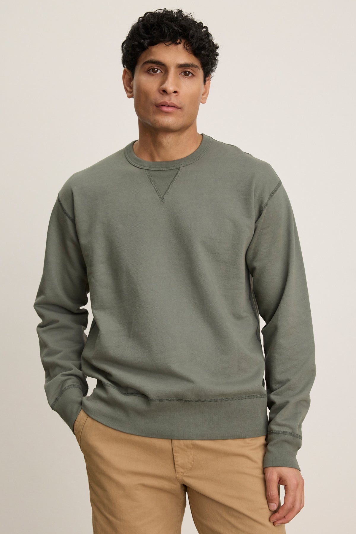 A man stands against a plain background wearing the RAE SWEATSHIRT by Velvet by Graham & Spencer in muted green French terry, paired with tan pants and hands in his pockets.-39446044573889
