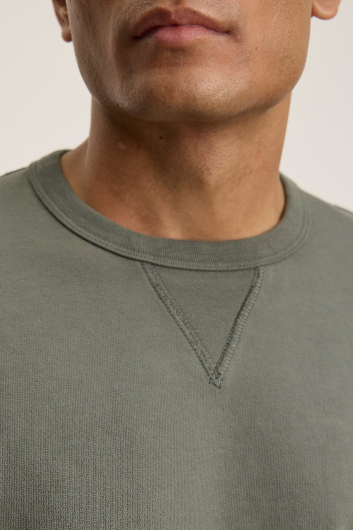 A close-up shows a person wearing the RAE SWEATSHIRT by Velvet by Graham & Spencer in olive green, featuring a classic crew neckline, with only the lower face and upper chest visible.-39446044704961
