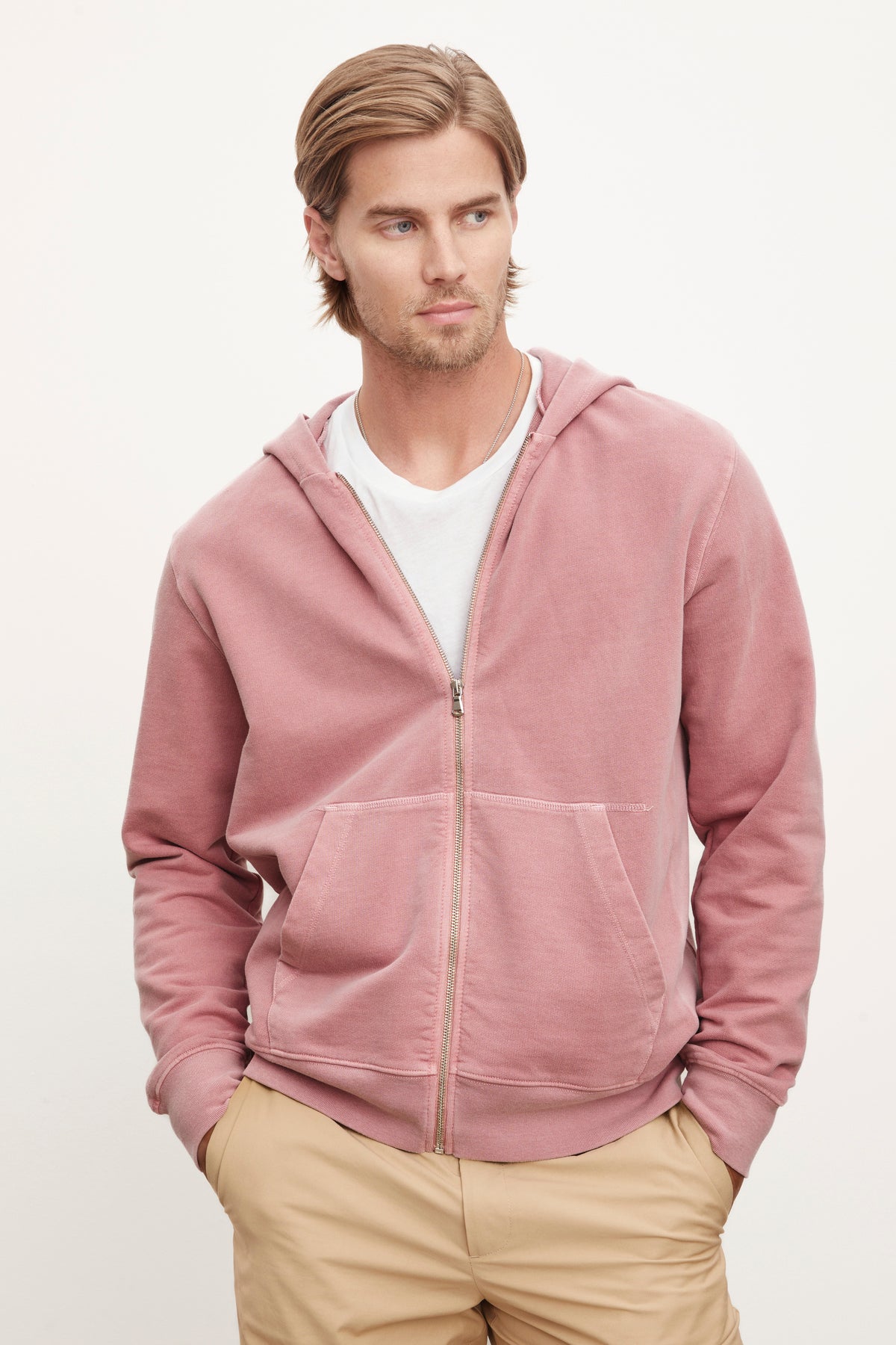   A man wearing a Velvet by Graham & Spencer VINCENT HOODIE in pink over a white t-shirt, paired with beige pants, posing against a plain background. 