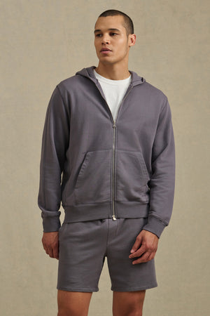A man wears the VINCENT HOODIE by Velvet by Graham & Spencer—a vintage-inspired light purple full-zip hoodie in soft French terry cotton—paired with a white t-shirt and matching shorts against a neutral background.