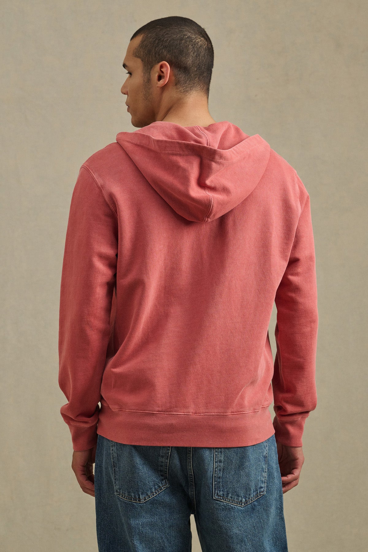 A person stands with their back to the camera, wearing the VINCENT HOODIE by Velvet by Graham & Spencer in vintage-inspired faded red, paired with blue jeans, set against a plain neutral background.-41428202979521