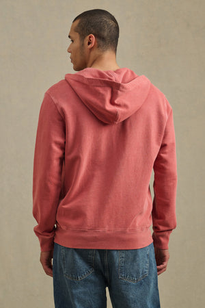 A person stands with their back to the camera, wearing the VINCENT HOODIE by Velvet by Graham & Spencer in vintage-inspired faded red, paired with blue jeans, set against a plain neutral background.