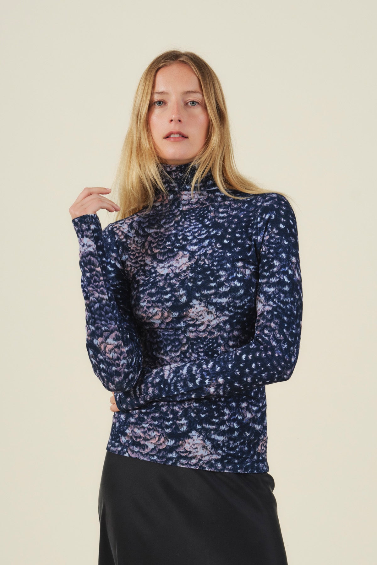 A person wearing a TAYLOR PRINTED TEE, a long-sleeved mock neck top in feather jersey fabric with a dark blue and purple abstract print.
