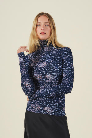 A person wearing a TAYLOR PRINTED TEE, a long-sleeved mock neck top in feather jersey fabric with a dark blue and purple abstract print.