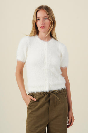 Soft, airy, white GABBY FEATHER YARN CARDIGAN with short sleeves buttoned to the neck, worn with olive green pants.