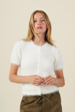 A person wearing a white, short-sleeved GABBY FEATHER YARN CARDIGAN by Velvet by Graham & Spencer, made of lightweight feather yarn and buttoned down the front.
