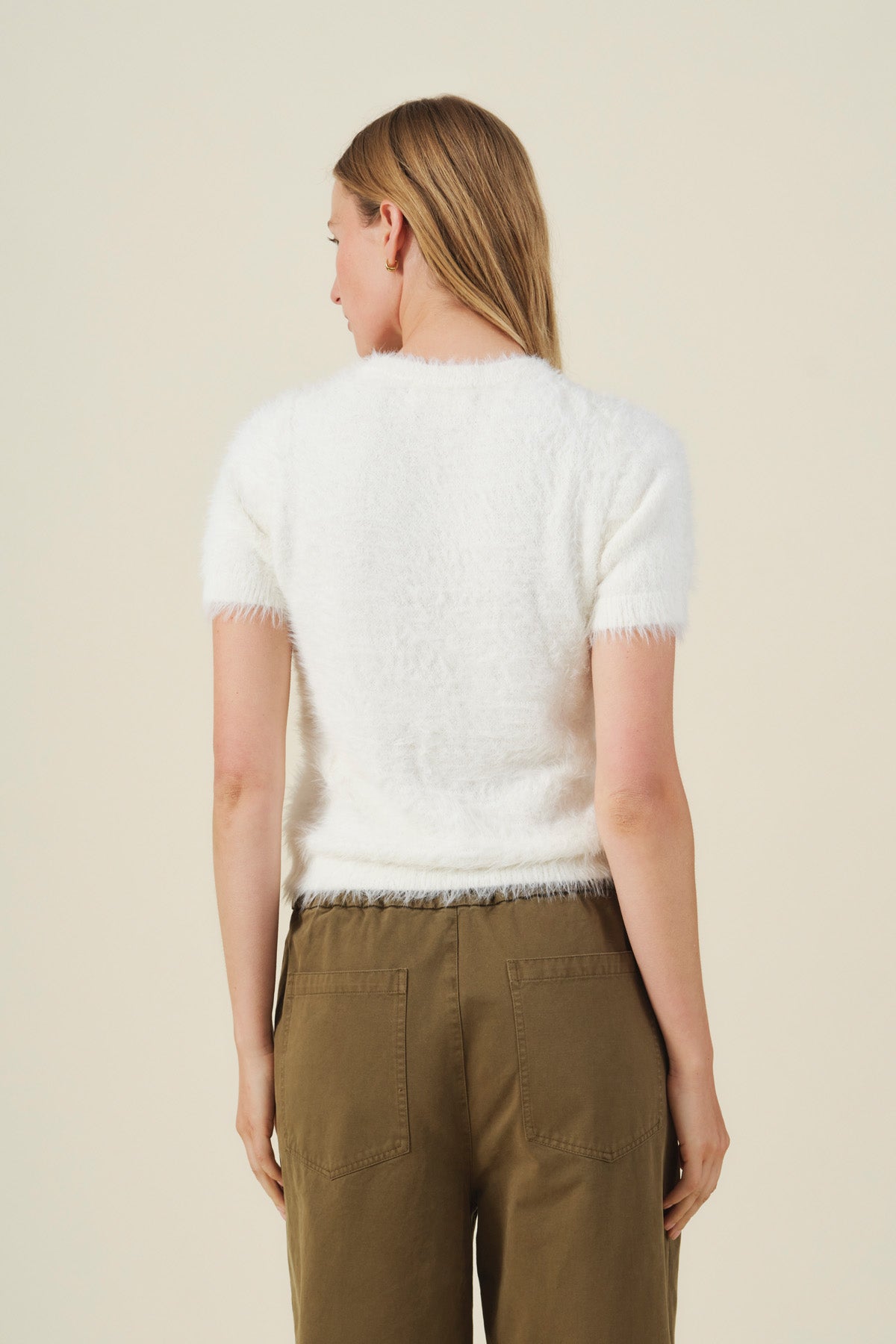 Back view of a white, short-sleeved, lightweight GABBY FEATHER YARN CARDIGAN paired with olive green pants.