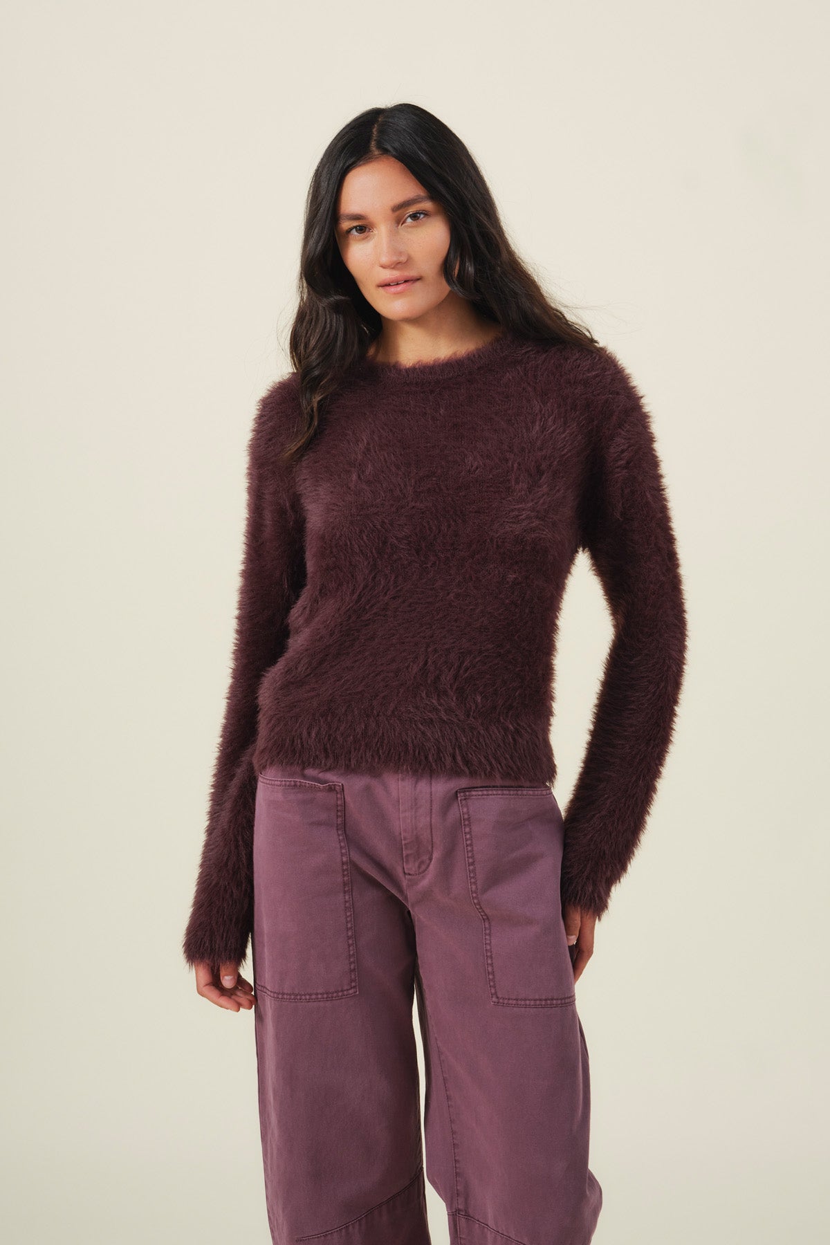 A person wearing a fuzzy, dark maroon PENNY FEATHER YARN SWEATER by Velvet by Graham & Spencer with a crew neckline and plum-colored pants with front patch pockets.