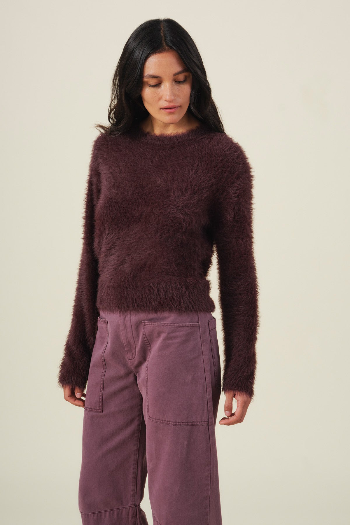 A woman wears a long-sleeved, fuzzy dark purple PENNY FEATHER YARN SWEATER in lightweight feather yarn with matching purple wide-leg pants.