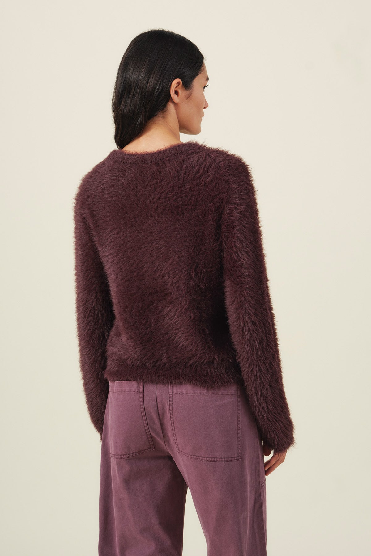 A person viewed from behind wearing a PENNY FEATHER YARN SWEATER, a long-sleeved, fuzzy dark purple sweater with a classic crew neckline.-46489576669377