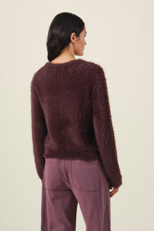 A person viewed from behind wearing a PENNY FEATHER YARN SWEATER, a long-sleeved, fuzzy dark purple sweater with a classic crew neckline.