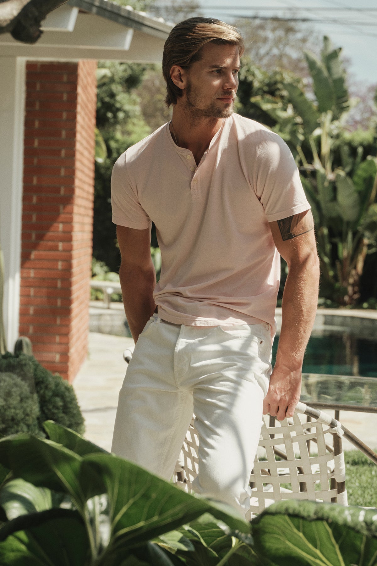   Fulton Short Sleeve Henley in light pink color bloom with white pants front view sitting outside 