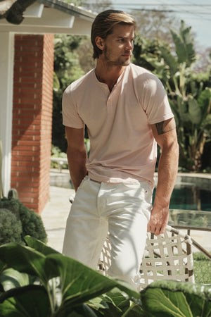 Fulton Short Sleeve Henley in light pink color bloom with white pants front view sitting outside