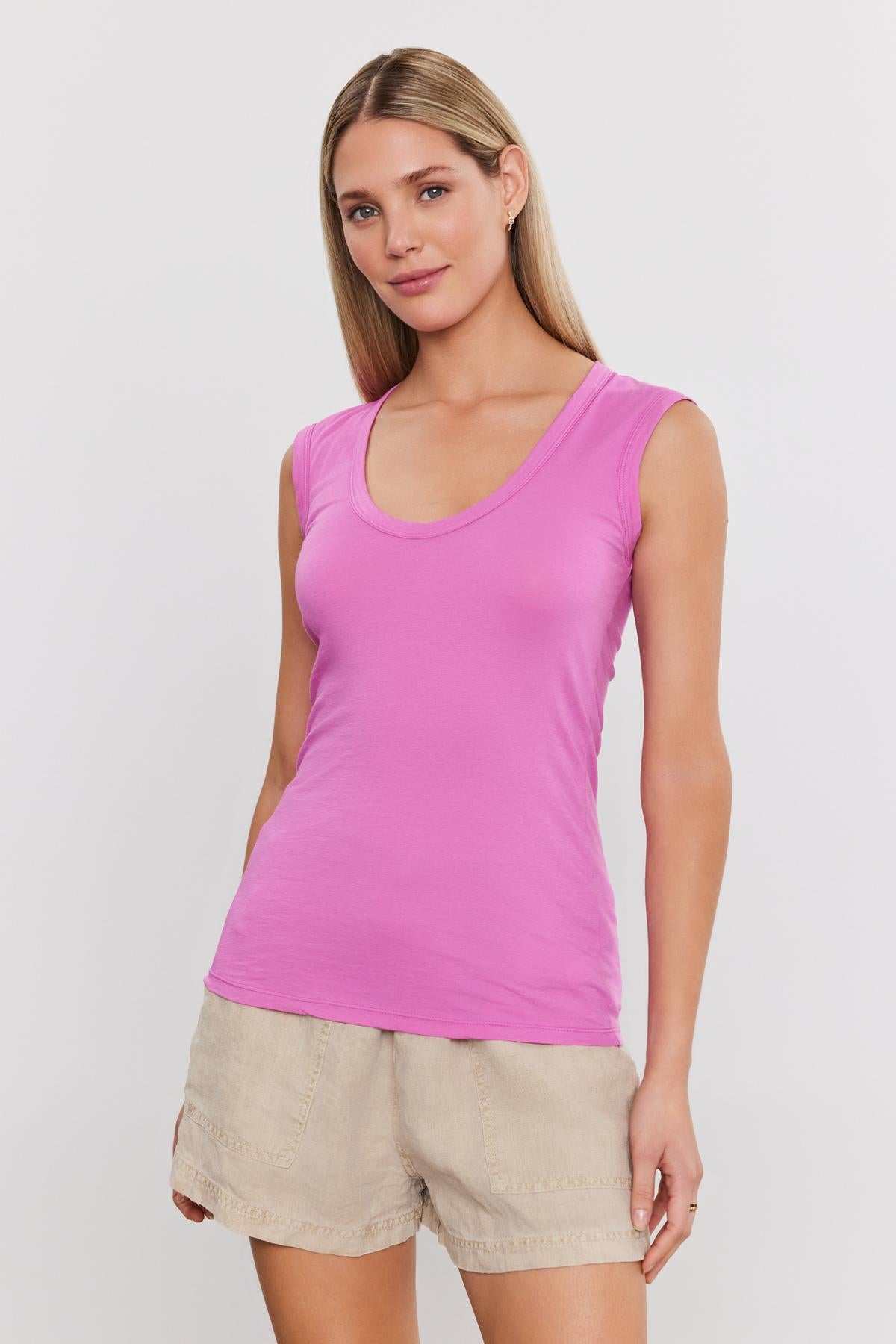 A woman wearing a bright pink ESTINA TANK TOP by Velvet by Graham & Spencer paired with beige shorts stands against a plain background.-37575445184705