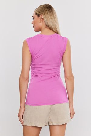 A blonde woman wearing a laid-back ESTINA TANK TOP by Velvet by Graham & Spencer and beige shorts is standing with her back to the camera.