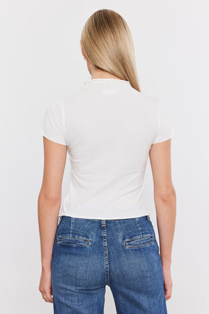 The back view of a woman wearing jeans and a white Velvet by Graham & Spencer Jackie Mock Neck Tee with a cropped silhouette.