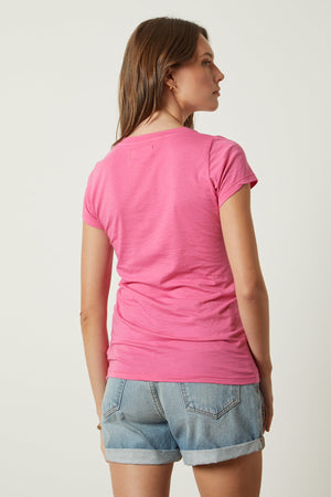 The back view of a woman wearing a Velvet by Graham & Spencer JEMMA GAUZY WHISPER FITTED CREW NECK TEE and denim shorts.