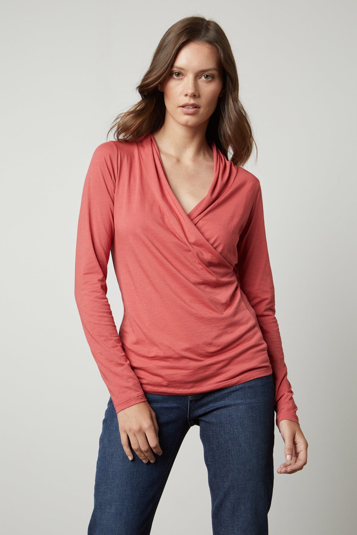 Woman wearing a Velvet by Graham & Spencer MERI WRAP FRONT FITTED TOP, coral long-sleeve top with a cross over v-neck and denim jeans.-36328493252801