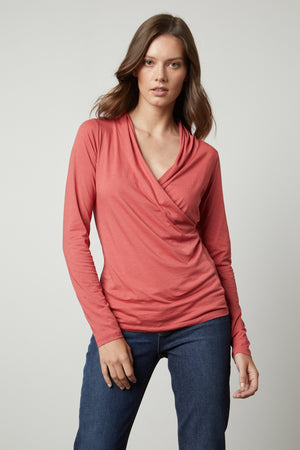 Woman wearing a Velvet by Graham & Spencer MERI WRAP FRONT FITTED TOP, coral long-sleeve top with a cross over v-neck and denim jeans.