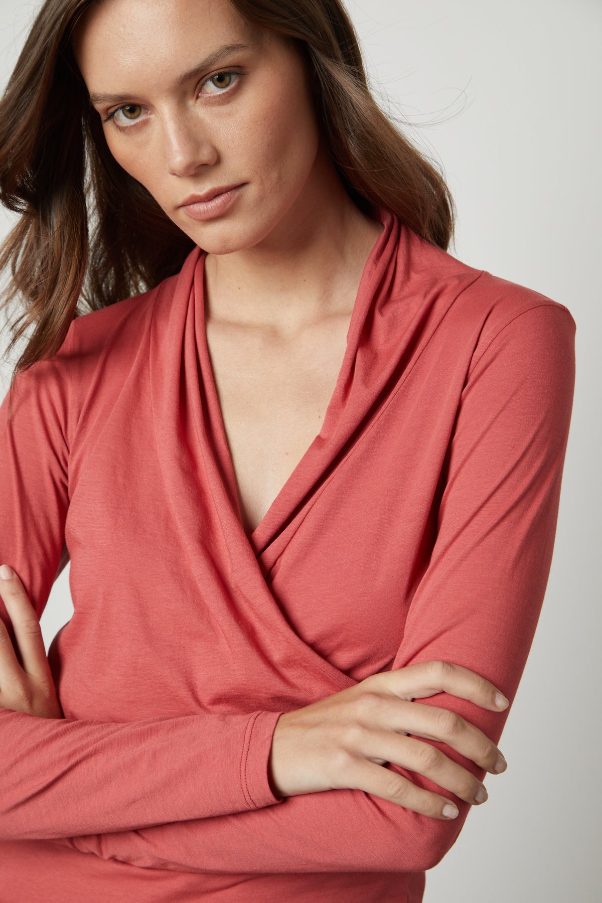   Woman wearing a rust-colored Velvet by Graham & Spencer MERI wrap front fitted top, posing with arms crossed. 