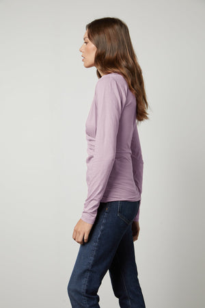 a woman wearing jeans and a long-sleeved MERI WRAP FRONT FITTED TOP in lavender by Velvet by Graham & Spencer.
