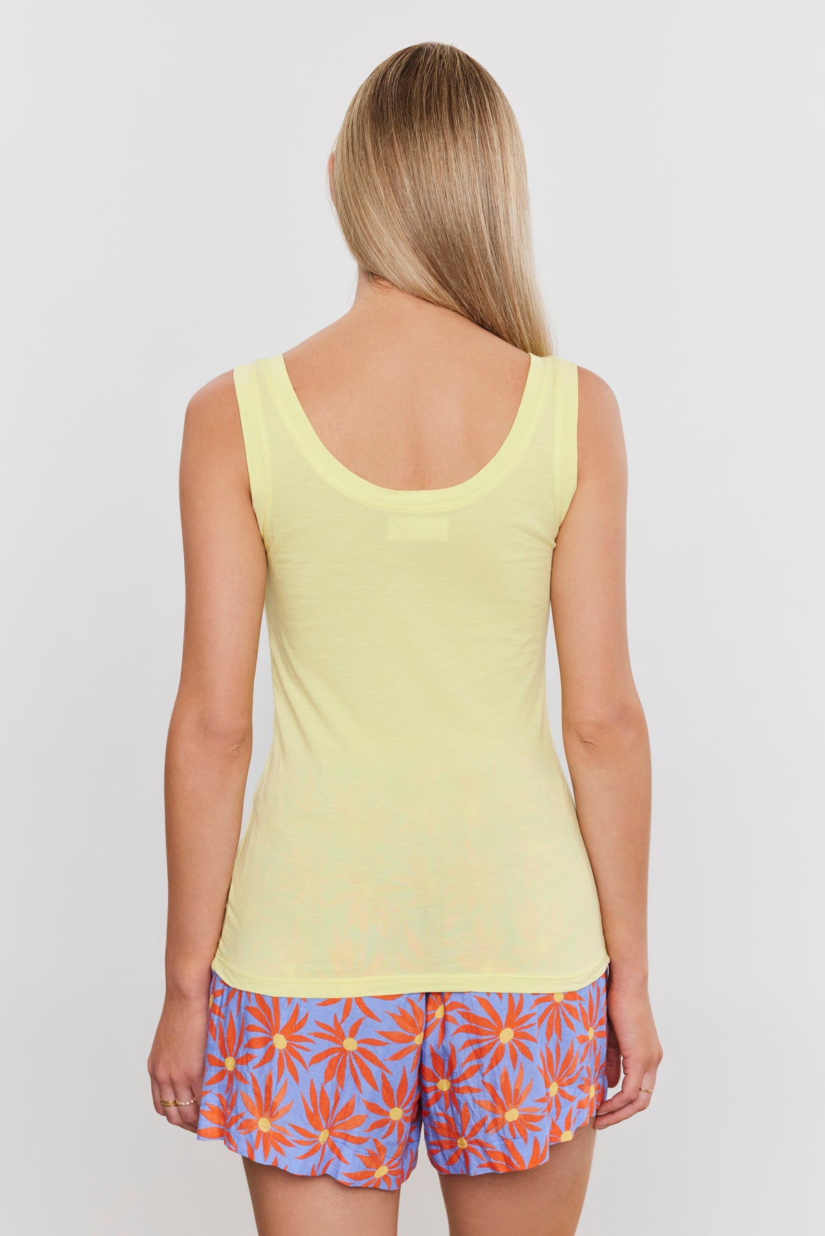 A woman seen from behind, wearing a Velvet by Graham & Spencer MOSSY GAUZY WHISPER FITTED TANK and colorful shorts with a leaf pattern.-36910237581505