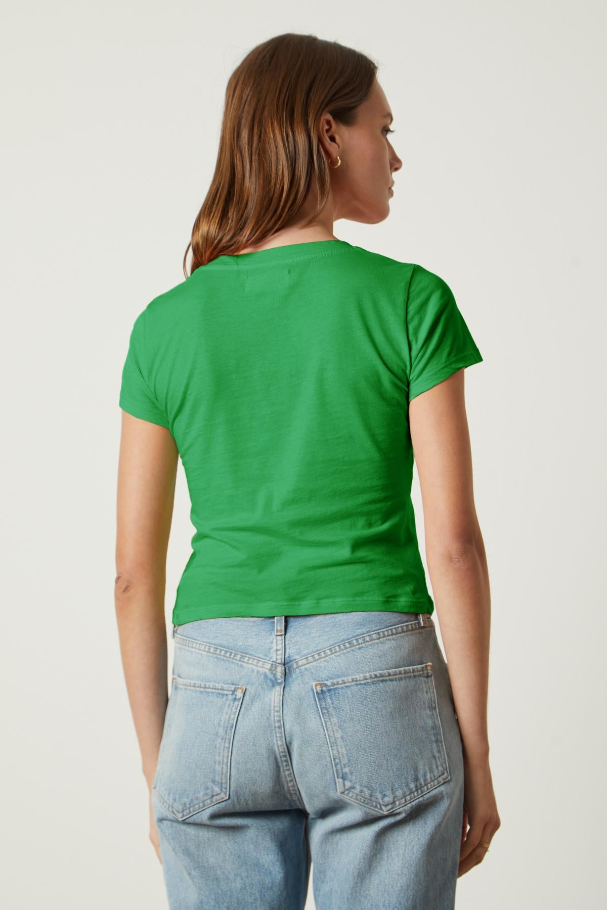   A person with long, light brown hair is wearing a green NINA TEE by Velvet by Graham & Spencer and light blue jeans, facing away from the camera. 