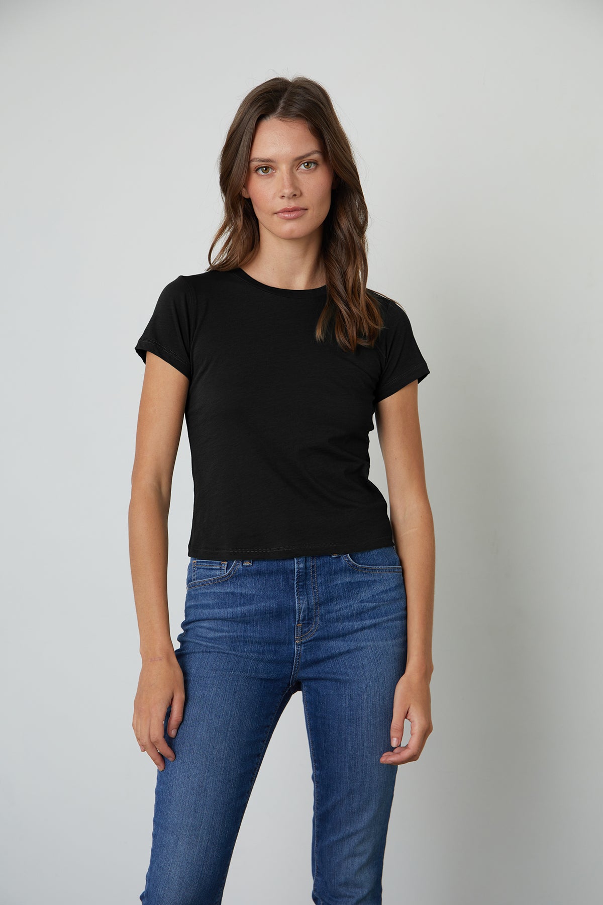   A woman donning a warm-weather Velvet by Graham & Spencer black whisper cotton knit Nina cropped crew neck tee paired with jeans. 