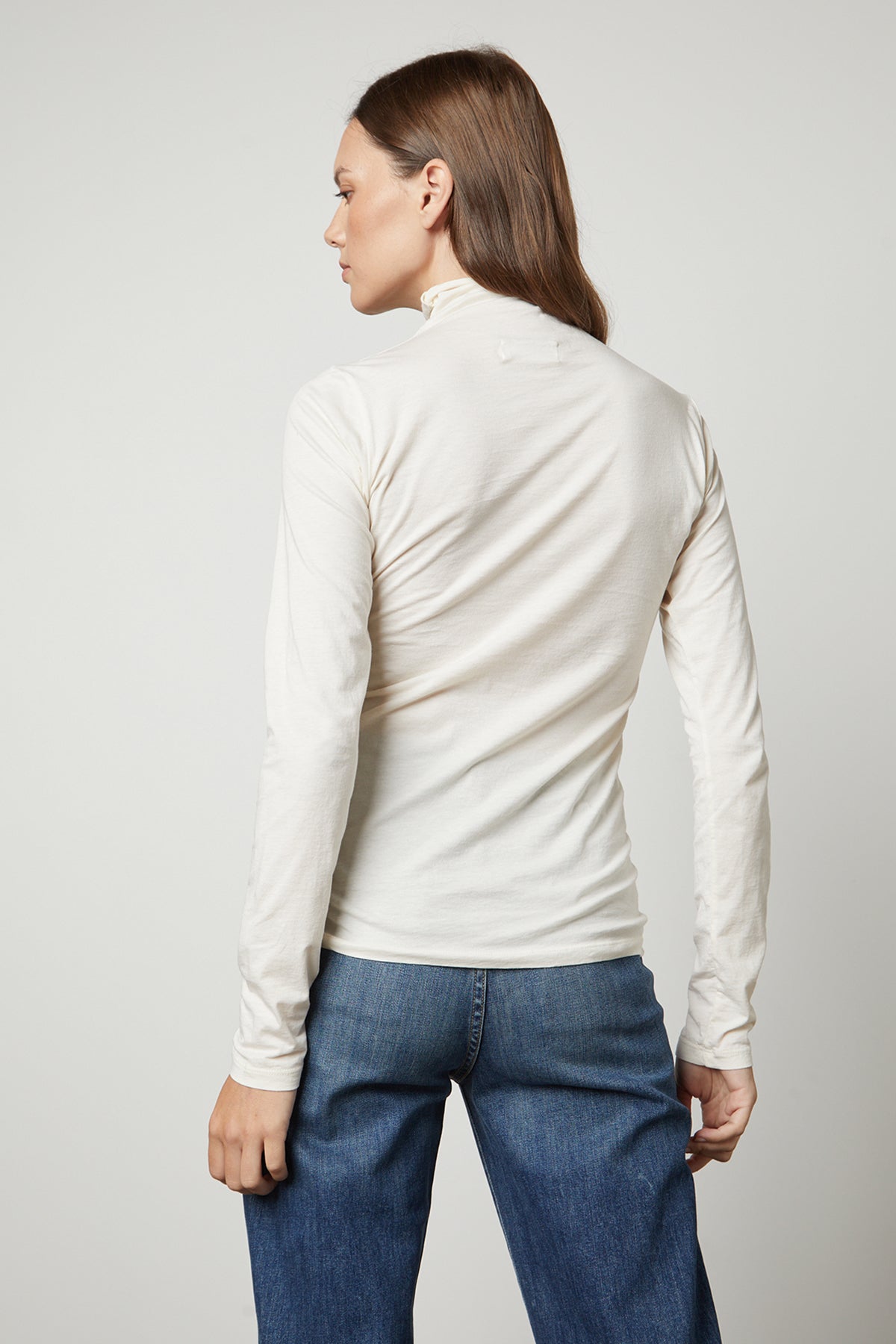 The back view of a woman flaunting a TALISIA GAUZY WHISPER FITTED MOCK NECK TEE by Velvet by Graham & Spencer and jeans, a wardrobe staple in the fashion world.-35230354178241