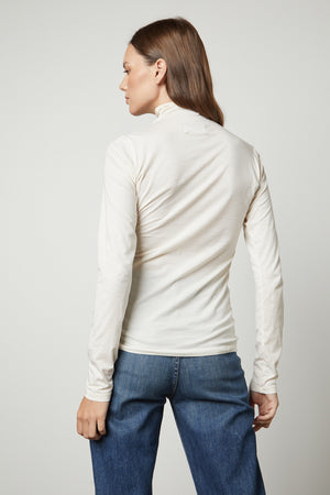 The back view of a woman flaunting a TALISIA GAUZY WHISPER FITTED MOCK NECK TEE by Velvet by Graham & Spencer and jeans, a wardrobe staple in the fashion world.
