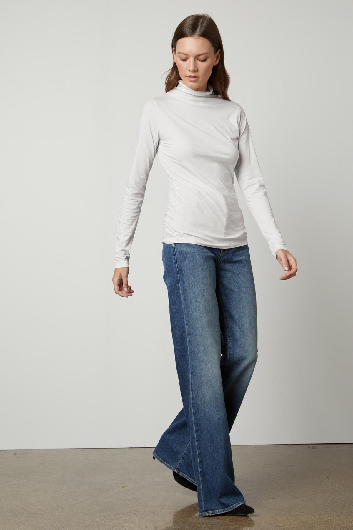   A woman wearing a versatile TALISIA GAUZY WHISPER FITTED MOCK NECK TEE and wide leg jeans that are popular in the fashion world, by Velvet by Graham & Spencer. 