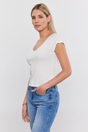 A woman in a Velvet by Graham & Spencer TOBY TEE and blue jeans standing against a white background, looking at the camera.