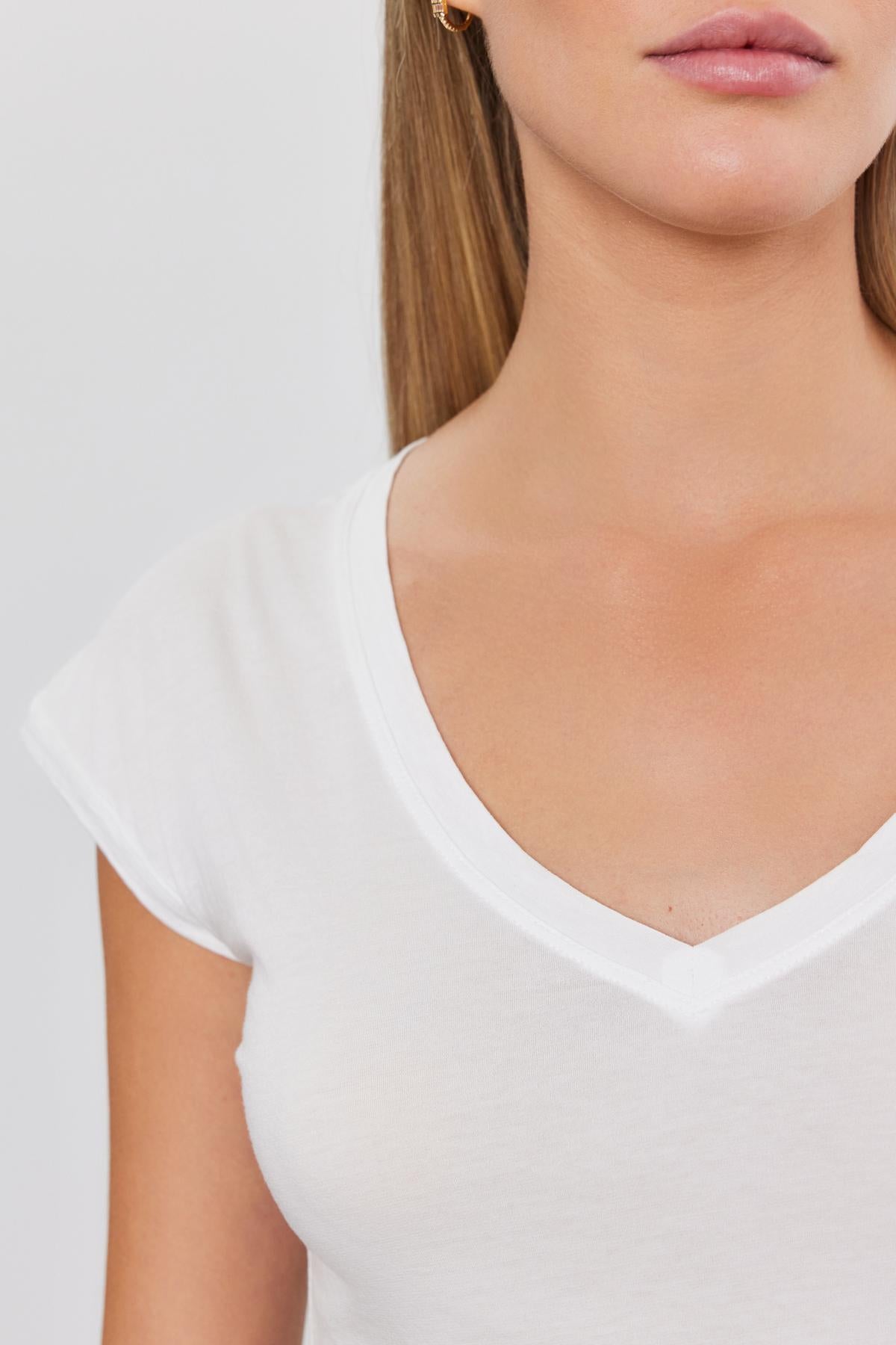Close-up of a woman wearing a white TOBY TEE v-neck t-shirt by Velvet by Graham & Spencer, focusing on the neckline and collar area.-36752997417153
