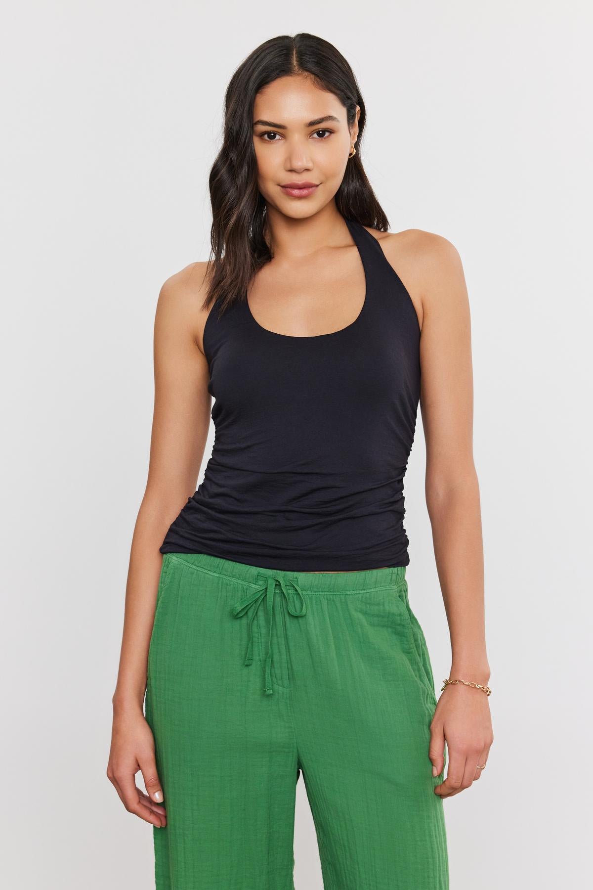   A woman standing against a white background wearing a WHITLEY TANK TOP by Velvet by Graham & Spencer and green pants. 