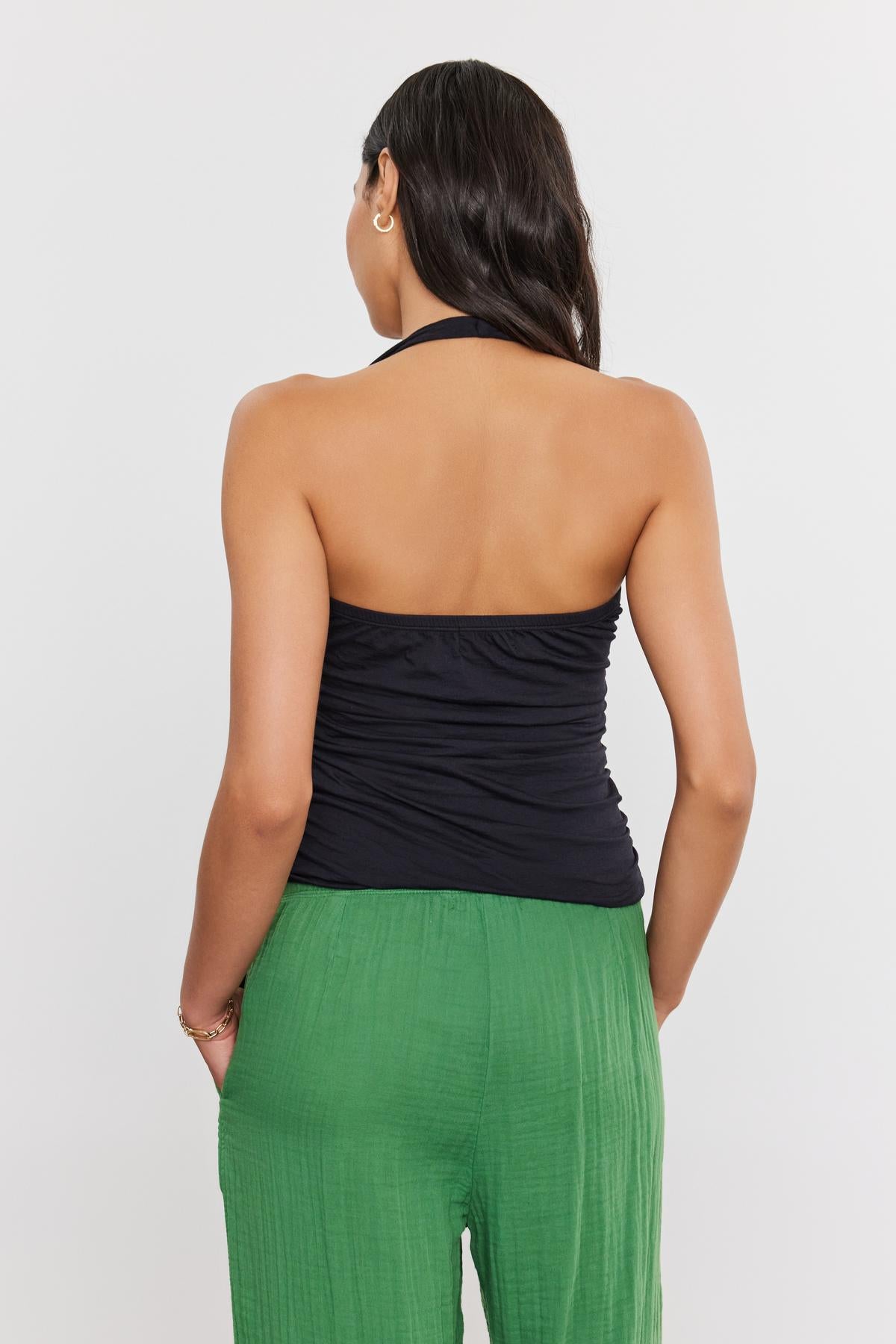   A person with long dark hair is shown from behind, wearing a Velvet by Graham & Spencer WHITLEY TANK TOP and green pants against a white background. 