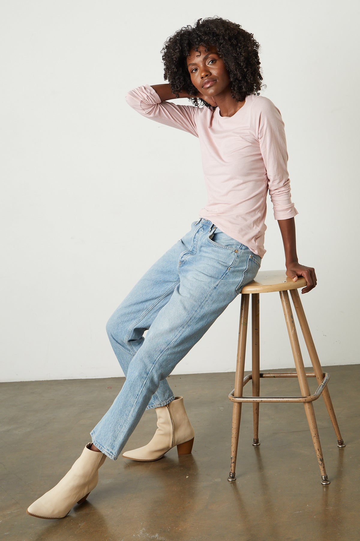   Model leaning on stool wearing Zofina Gauzy Whisper Fitted Crew Neck Tee with long sleeves in light pink ribbon color and light blue denim and cream boots front & side  