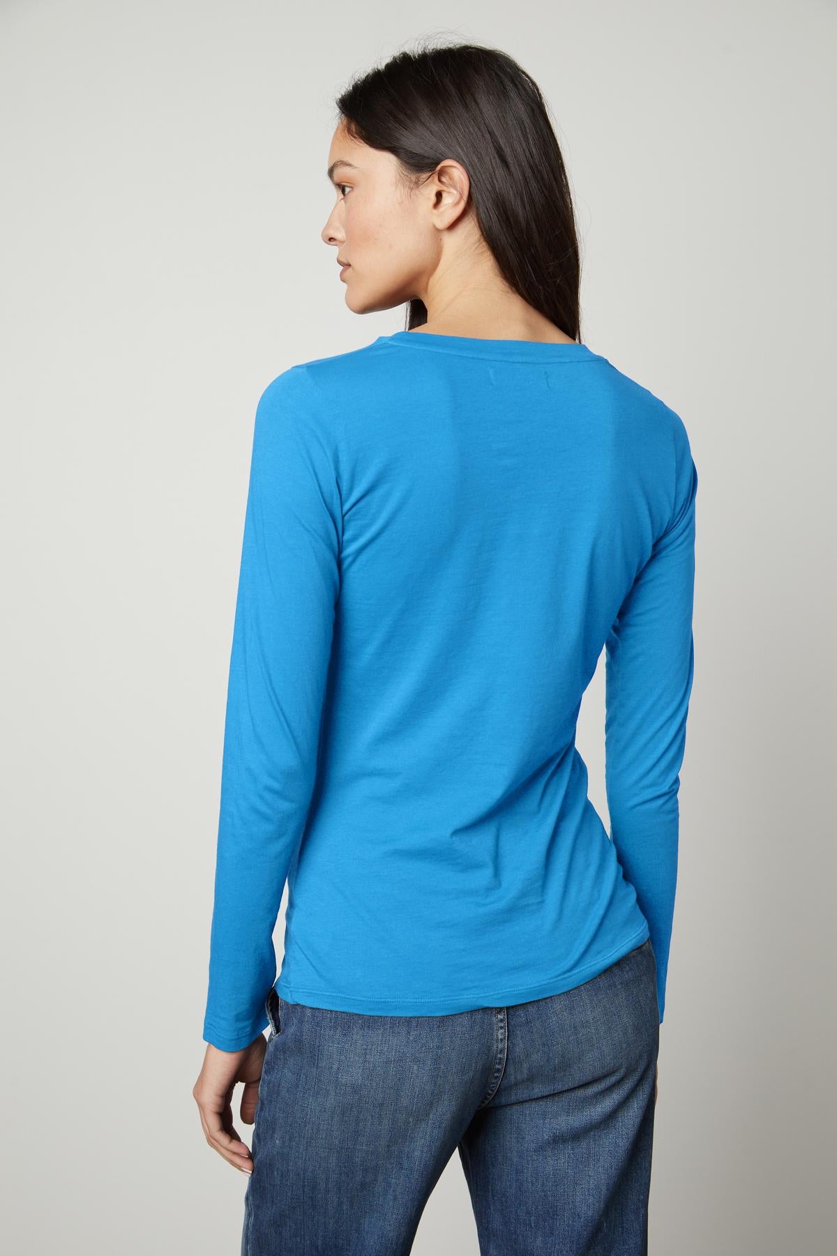 The back view of a woman wearing a Velvet by Graham & Spencer ZOFINA GAUZY WHISPER FITTED CREW NECK TEE, blue long-sleeve tee.-35503495381185