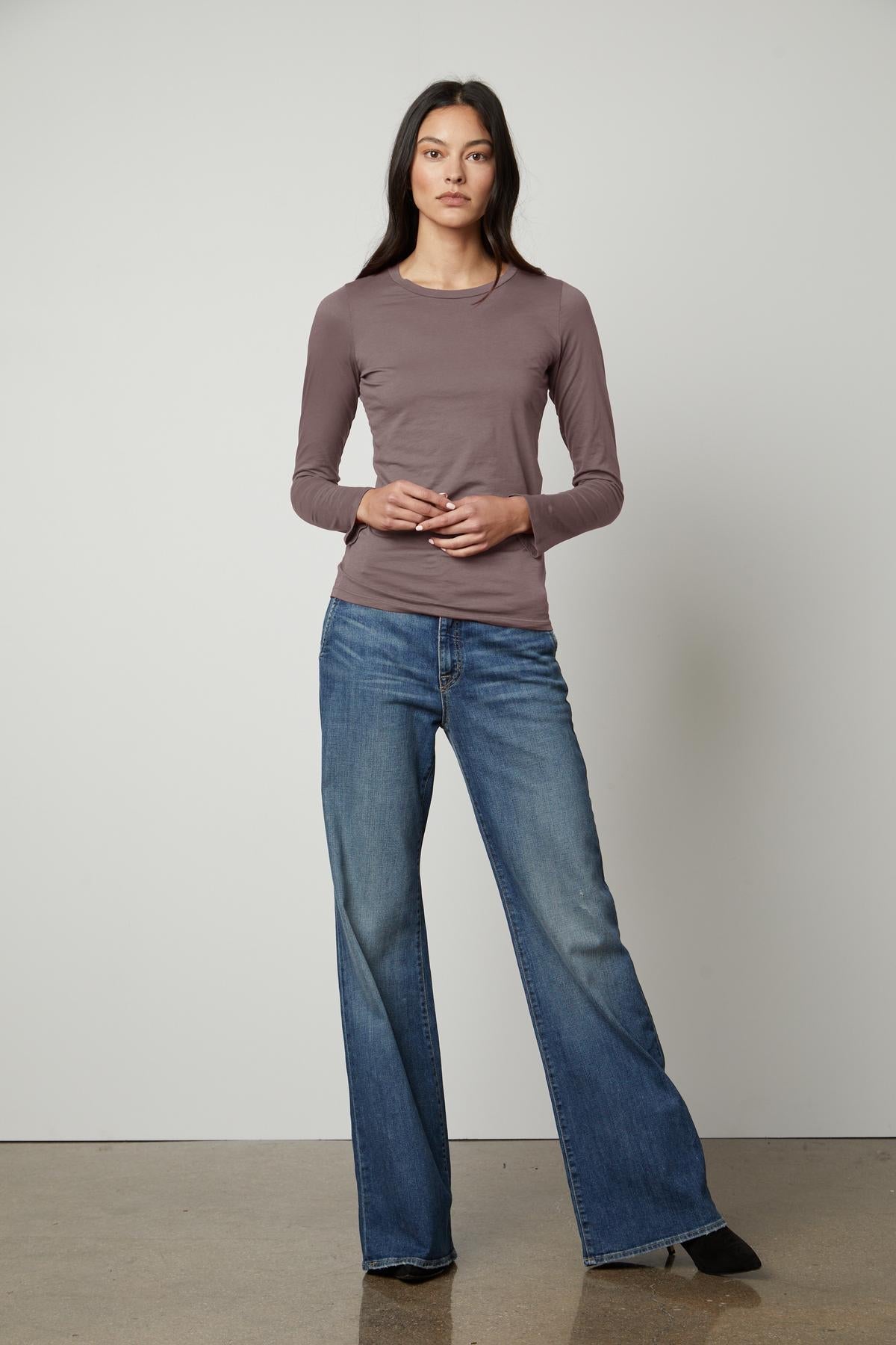   The model is wearing a Velvet by Graham & Spencer ZOFINA GAUZY WHISPER FITTED CREW NECK TEE top and flared jeans. 