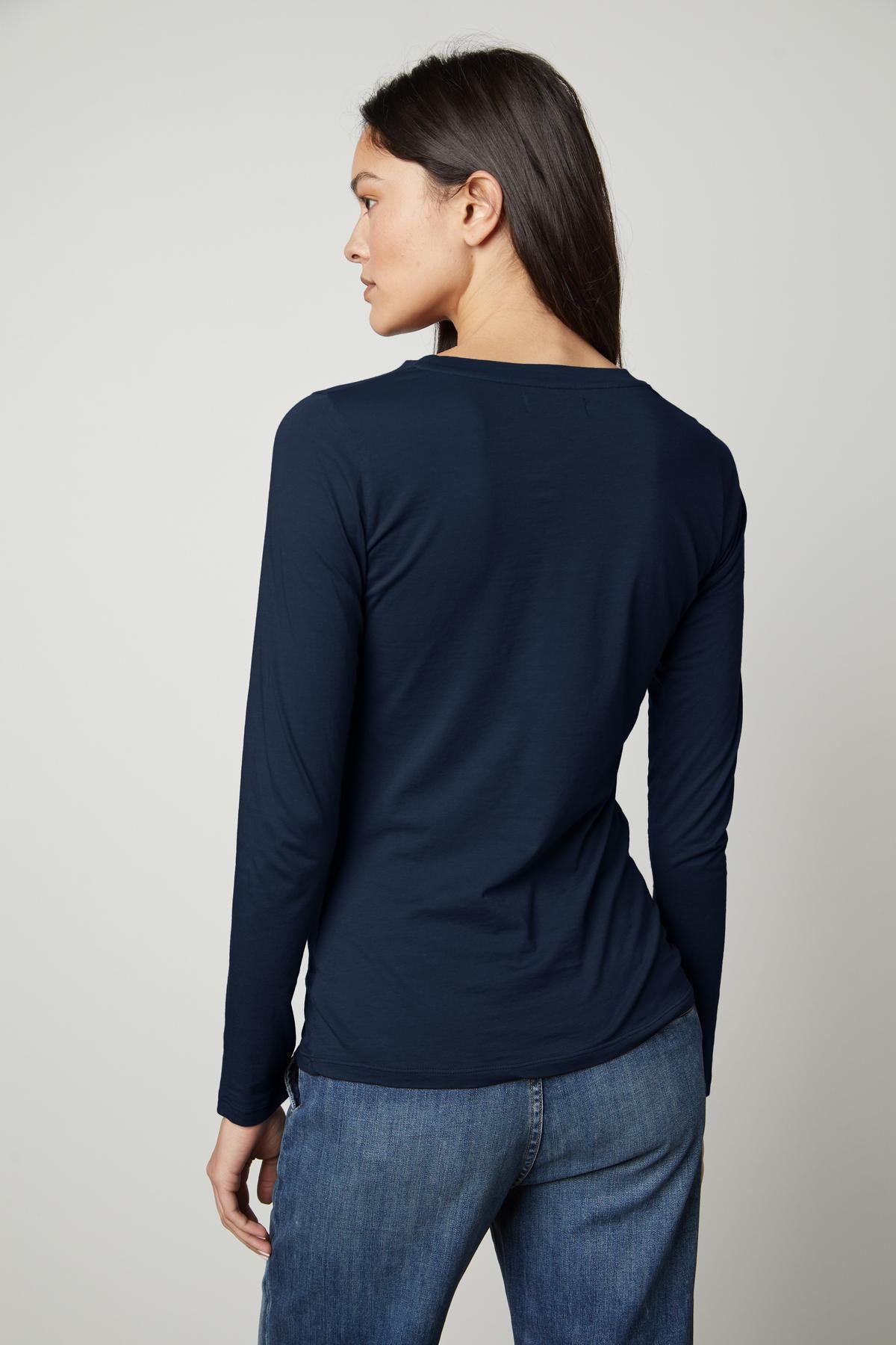 The back view of a woman wearing jeans and a Velvet by Graham & Spencer ZOFINA GAUZY WHISPER FITTED CREW NECK TEE.-35503491023041