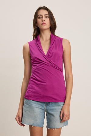 A woman in the ADELISE WRAP TANK by Velvet by Graham & Spencer and light blue denim shorts stands against a plain light-colored background.