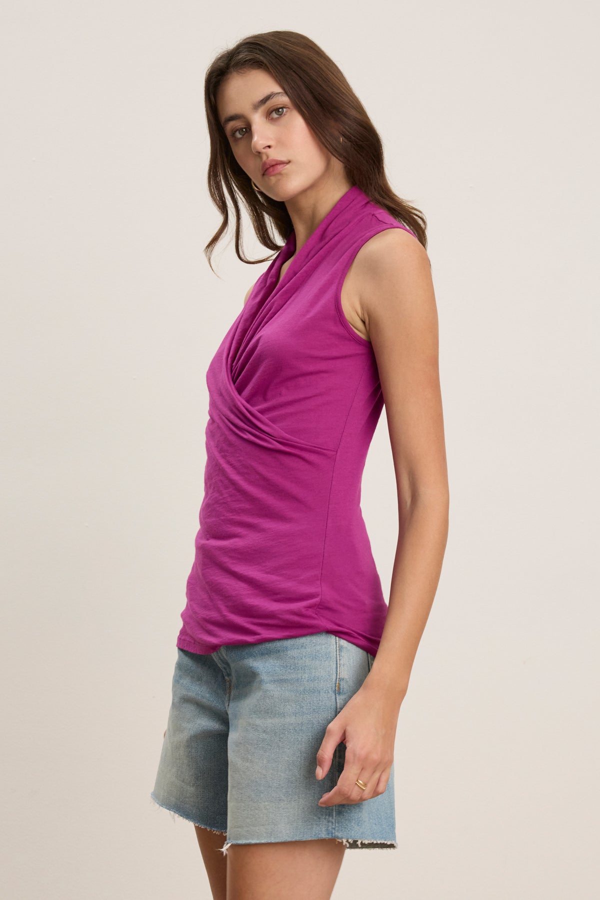 A woman stands slightly sideways against a plain light background, wearing the ADELISE WRAP TANK by Velvet by Graham & Spencer with light blue denim shorts.-39488754483393