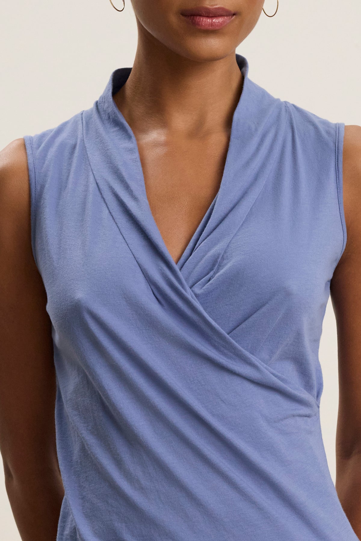   A woman wearing the ADELISE WRAP TANK by Velvet by Graham & Spencer, a sleeveless V-neck top with a wrap front detail, paired with small hoop earrings. 