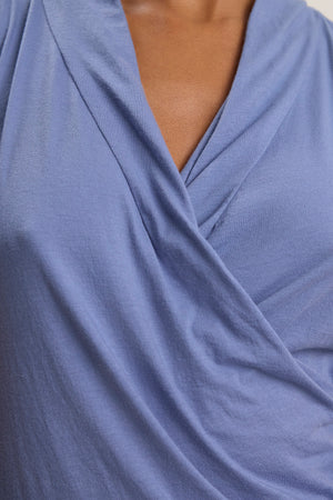 Close-up of a person wearing the ADELISE WRAP TANK by Velvet by Graham & Spencer, featuring a blue wrap front design with a V-shaped neckline.