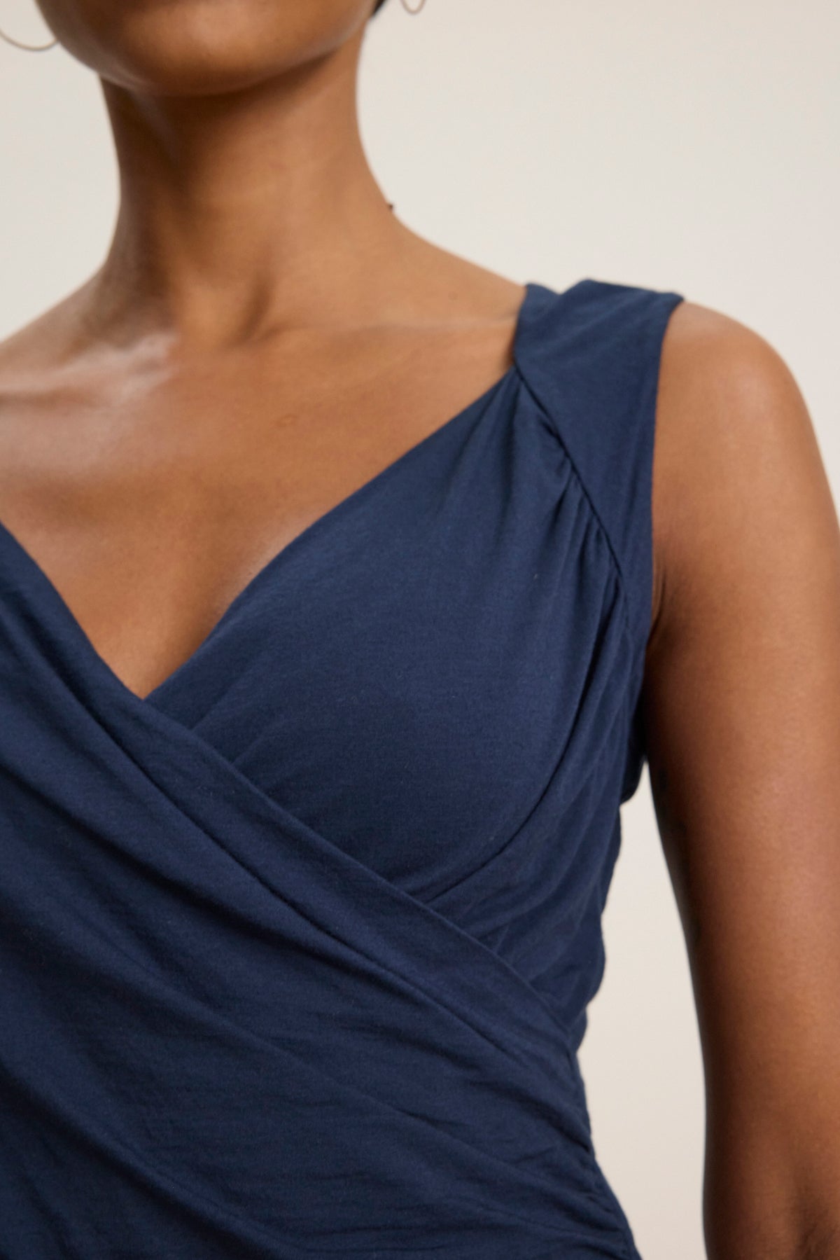 A person wearing the AZURA TANK TOP by Velvet by Graham & Spencer—a sleeveless, dark blue crossover wrap top with a form-fitting silhouette—shown from shoulders to waist against a plain background.-39119703572673