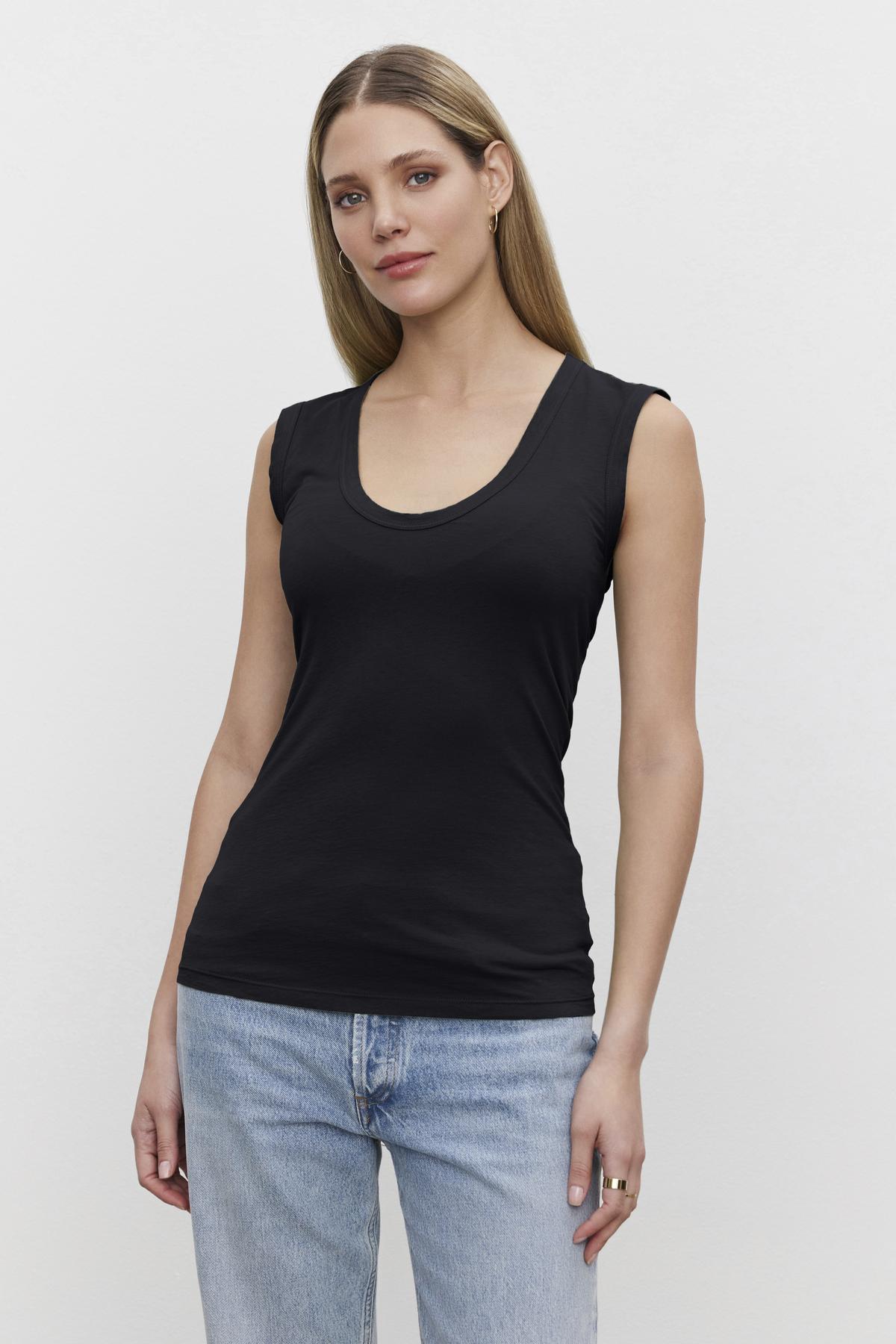 A woman with long hair wearing the ESTINA TANK TOP by Velvet by Graham & Spencer and blue jeans stands against a plain white background.-38426810319041