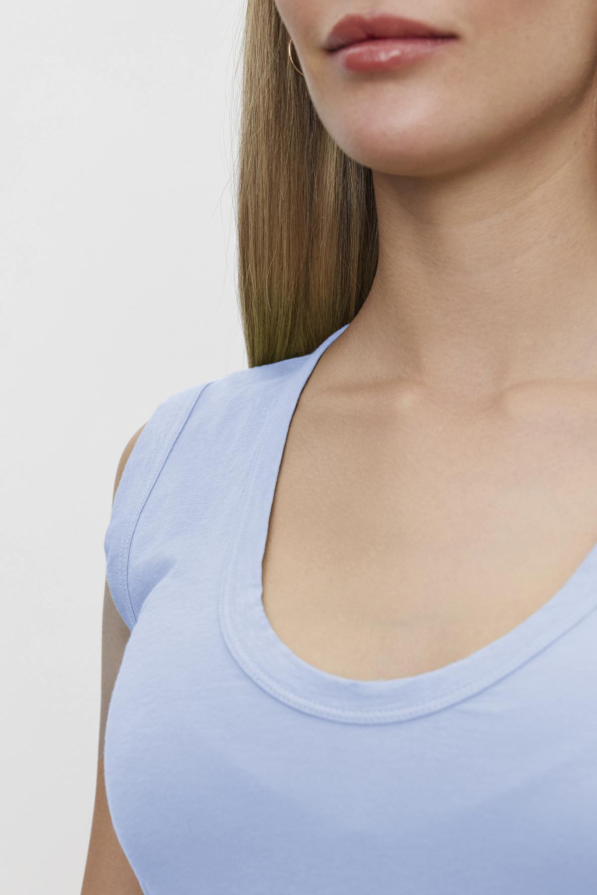   Close-up of a woman in a ESTINA GAUZY WHISPER FITTED TANK TOP by Velvet by Graham & Spencer, showing her neckline and long brown hair, against a white background. 
