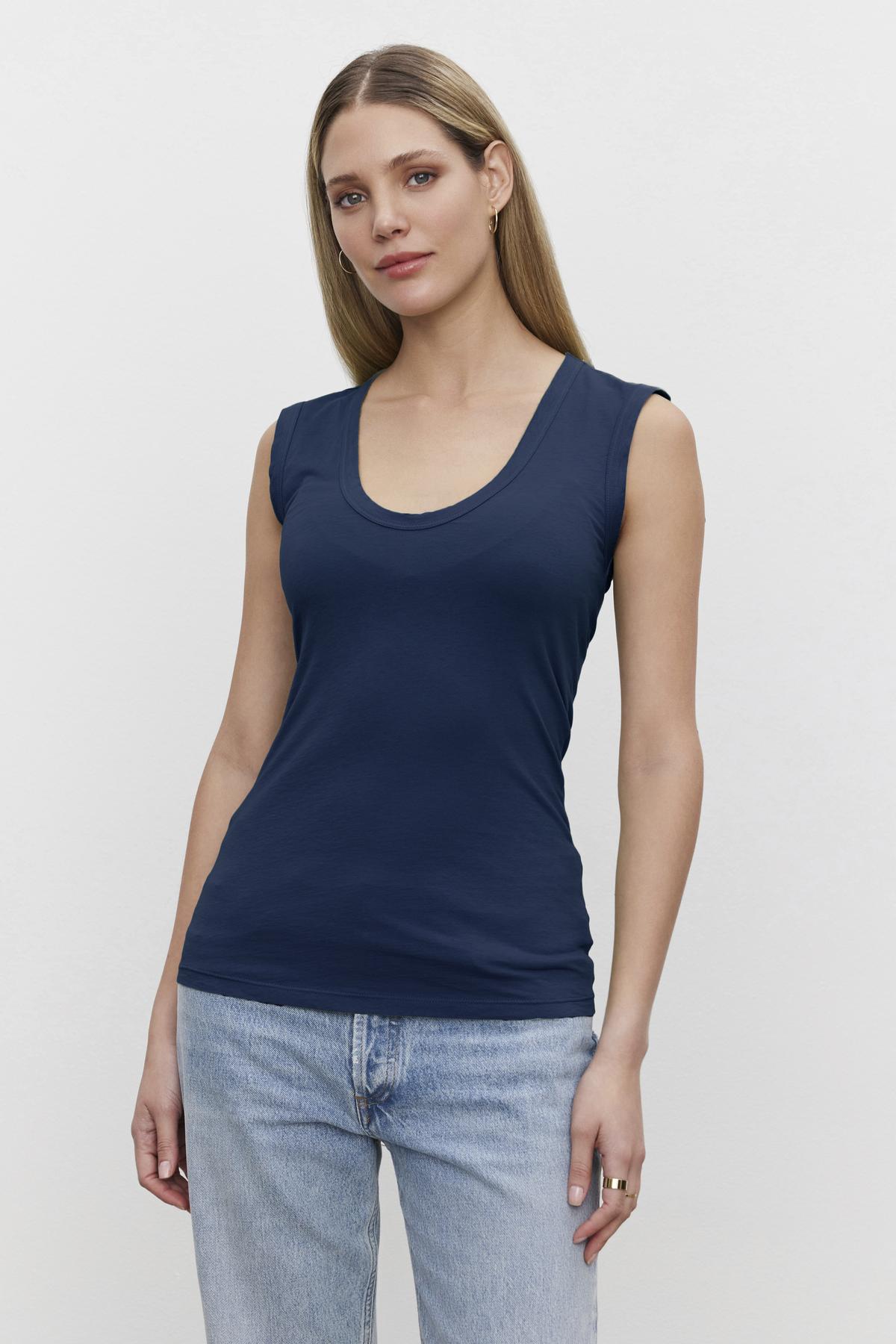   A woman in a navy ESTINA GAUZY WHISPER FITTED TANK TOP by Velvet by Graham & Spencer and jeans. 